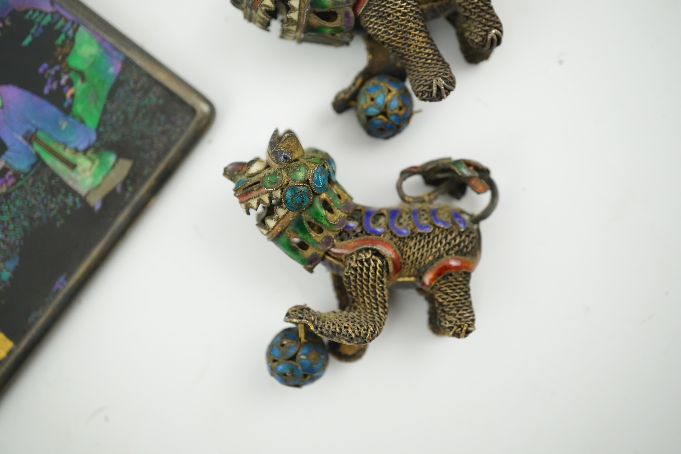 A Chinese silver buckle with filligree butterfly decoration, a pair of enamelled miniature lion dogs with balls and a small lac burgaute panel. Lion dogs 4.5cm long. Condition - good